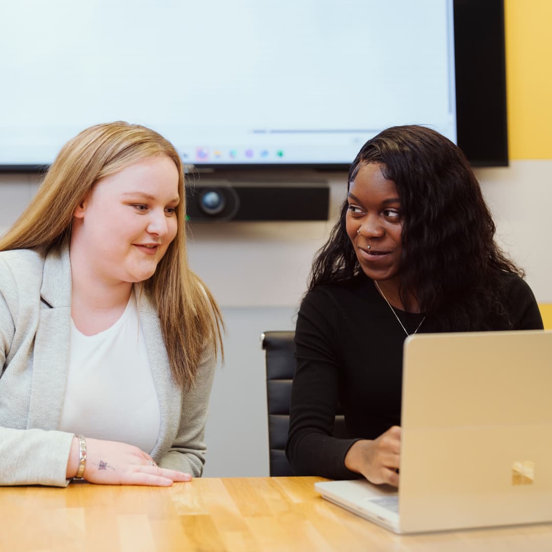 Two people working together at a laptop during a meeting, discussing work in a modern office environment.