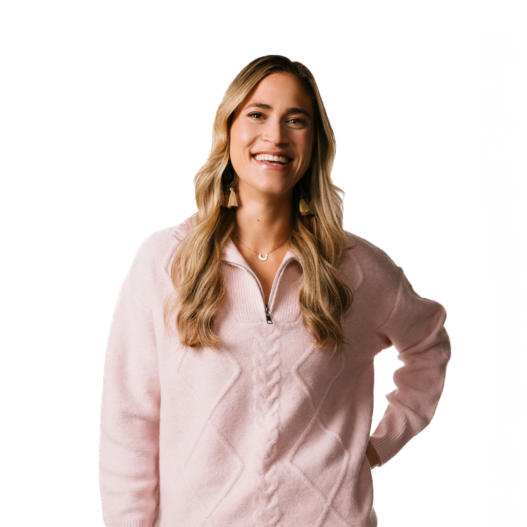 A young women with long blonde hair. She is smiling at the camera and has her hand on her hip. She is wearing a light pink jumper.