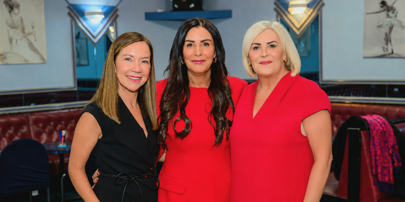 Three attendees standing together at a Brilliant Breakfast fundraising event, posing for a group photo in a venue decorated for the occasion.